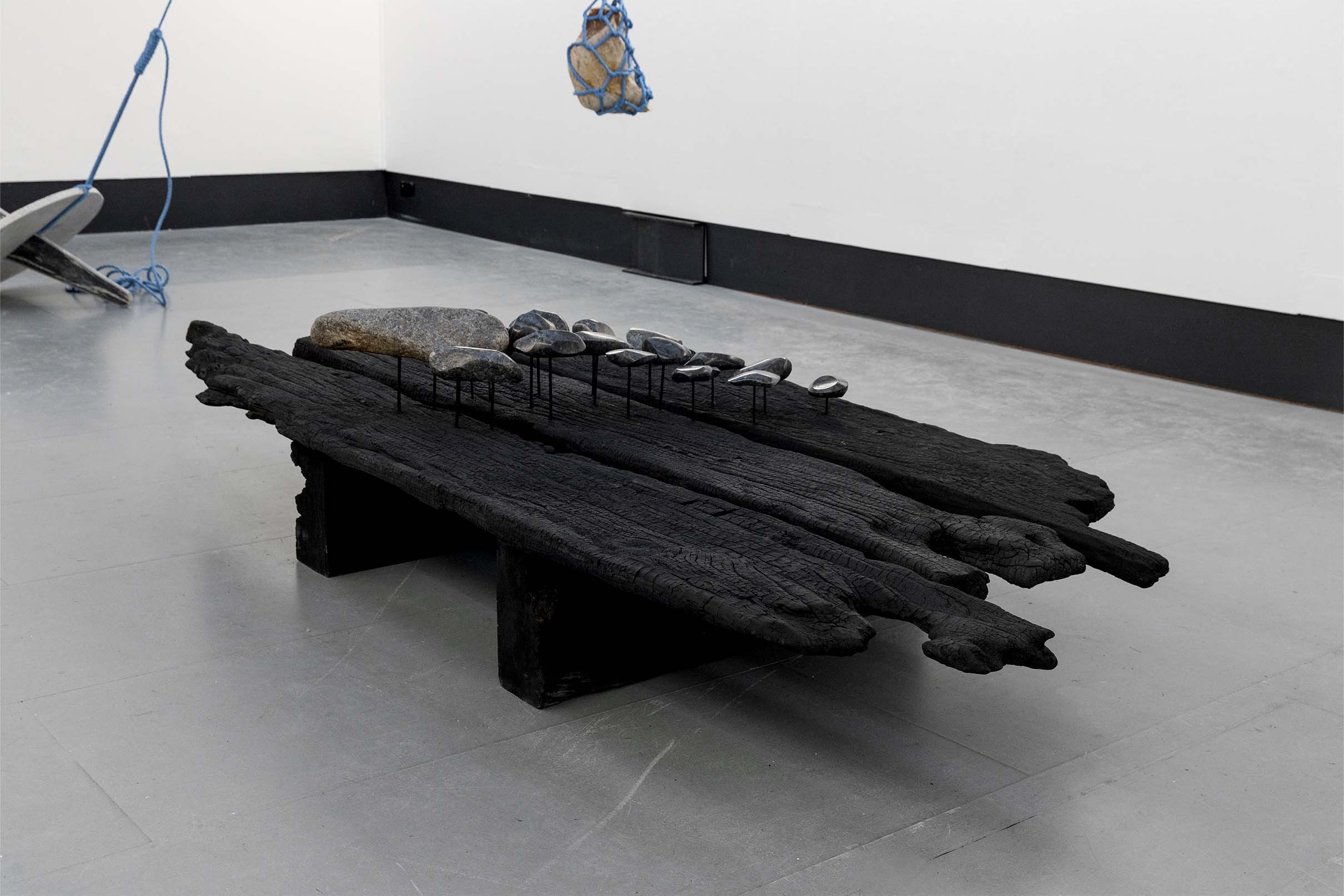 Ginnungagap by Sean Alec Auld. Polished stones raised on painted nails, on a charred wooden surface.