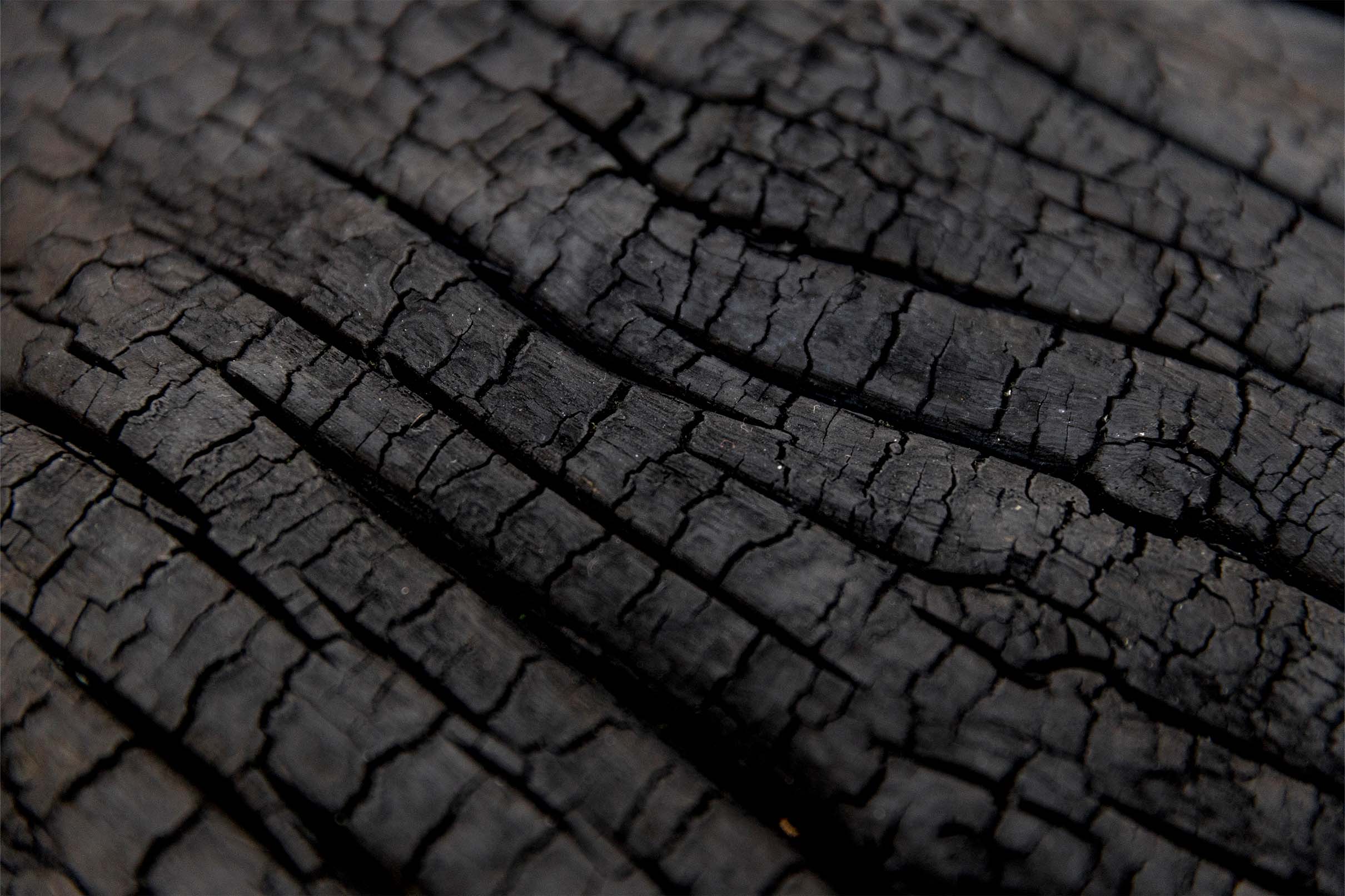 Close-up of Ginnungagap by Sean Alec Auld. Polished stones raised on painted nails, on a charred wooden surface.