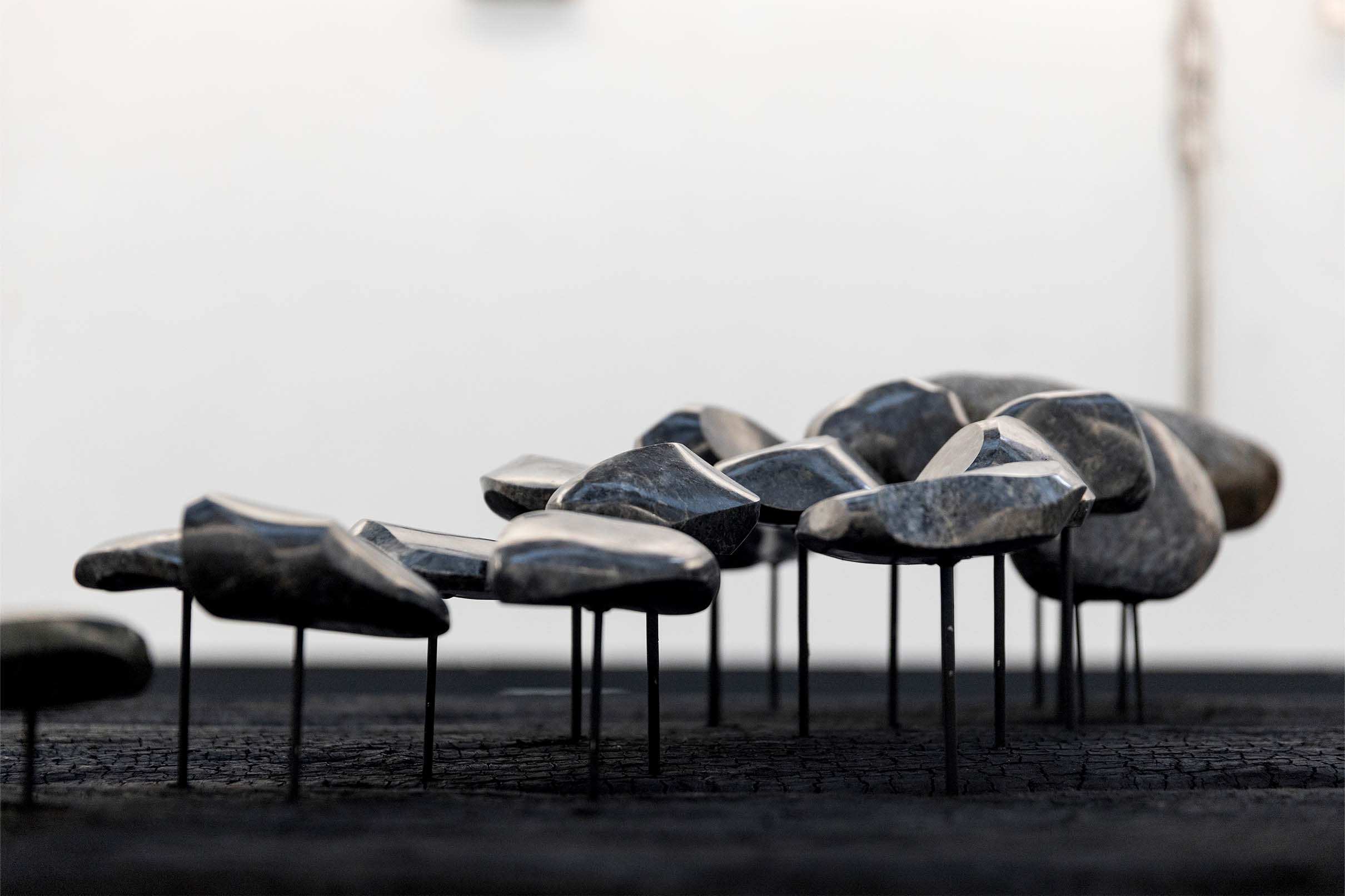 Close-up of Ginnungagap by Sean Alec Auld. Polished stones raised on painted nails, on a charred wooden surface.