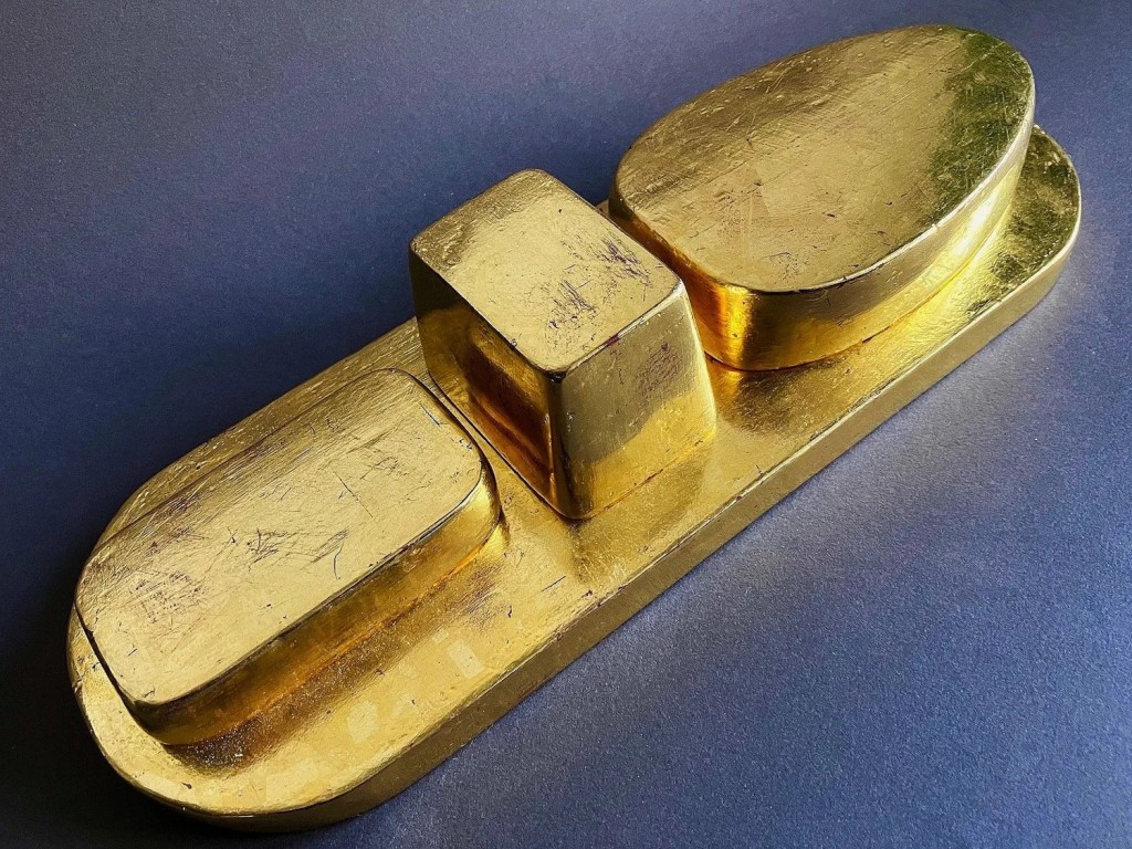 A gold sculpture called 'Cannery Row'; a base with raised shapes each resembling the shape of various cans, all finished with gold leaf. 